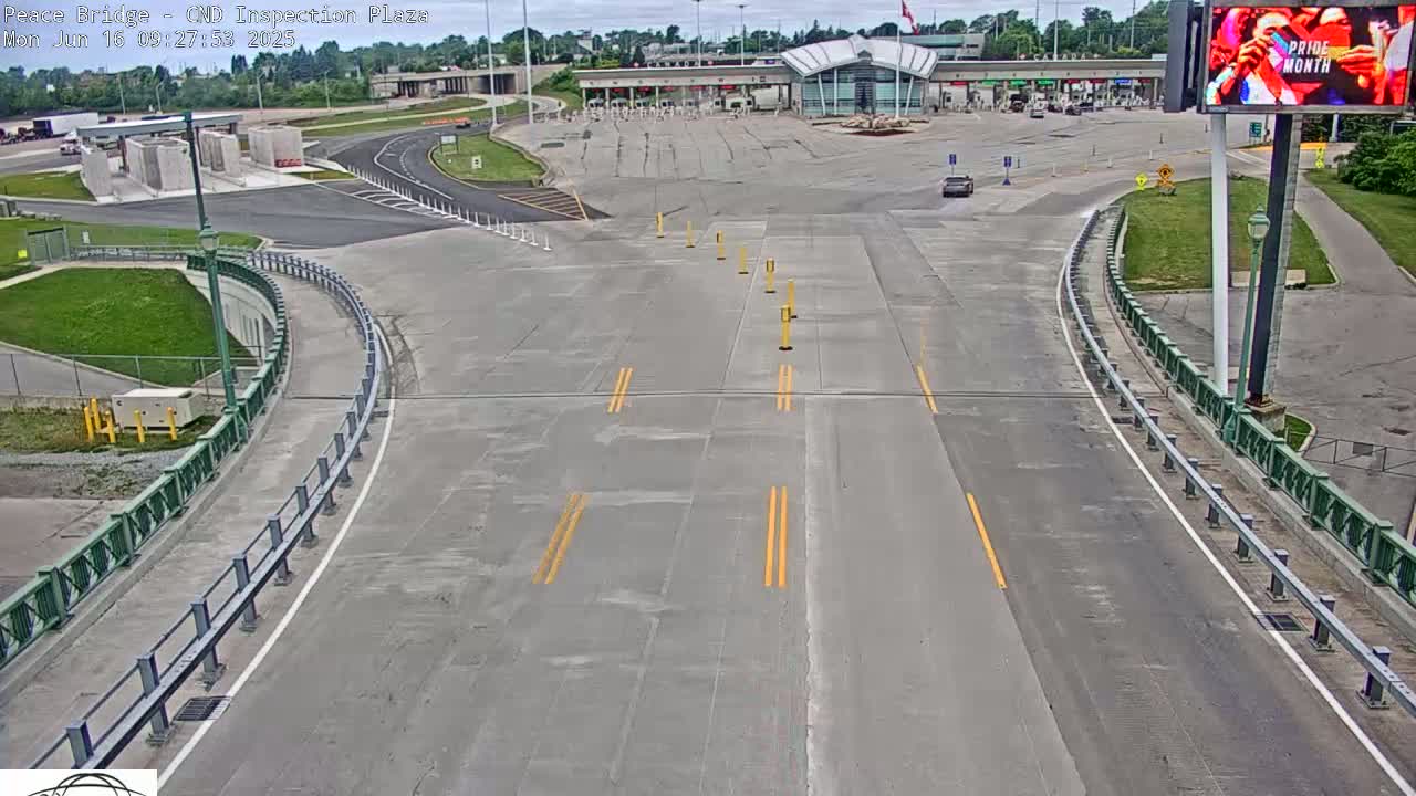 A mostly empty roadway curves toward a border inspection plaza under a partly cloudy sky.