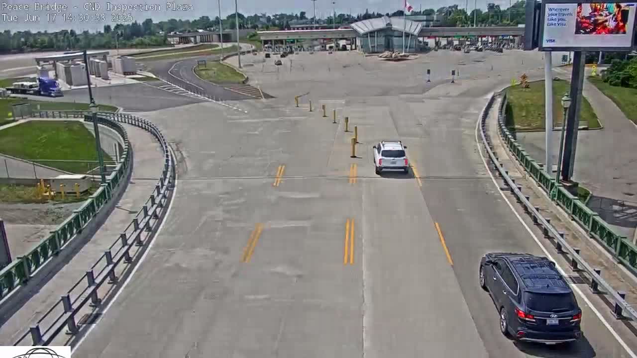 A mostly empty border inspection plaza with two vehicles on the roadway under a sunny sky.