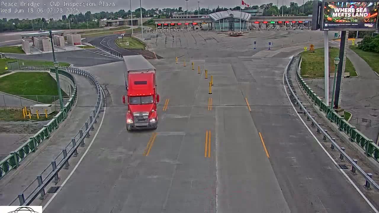 A red semi-truck drives toward a border inspection plaza on an overcast day.