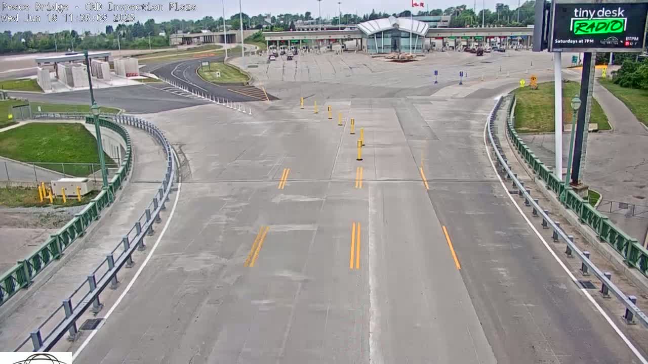 A mostly empty highway approaches a border inspection plaza on an overcast day.