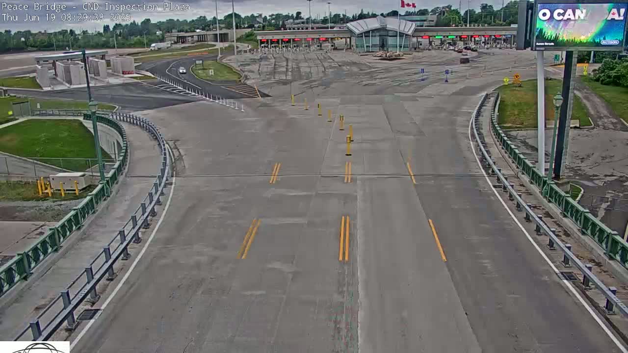 An overhead view shows a mostly empty border inspection plaza on an overcast day, with a roadway curving toward the inspection booths.
