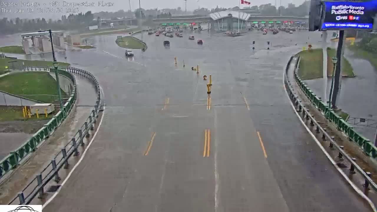 A rain-soaked roadway curves around a flooded inspection plaza with a few vehicles visible.
