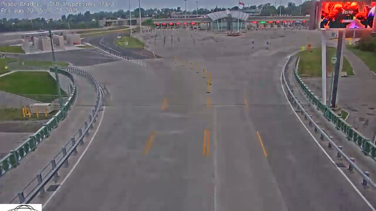 An empty border inspection plaza with a mostly gray sky is seen from a high vantage point, showing roadways curving toward the inspection booths.