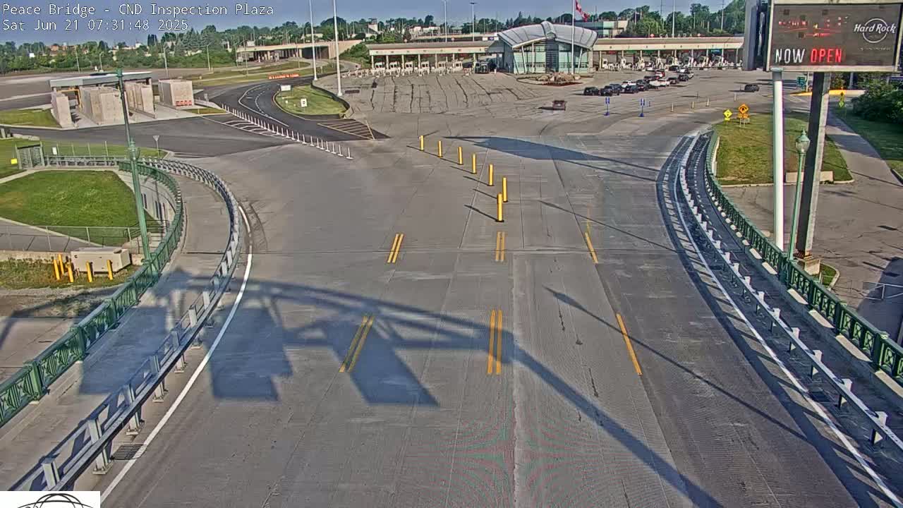 A mostly empty roadway curves toward a border crossing inspection plaza on a sunny day.