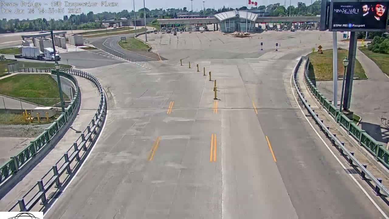A mostly empty highway approaches a border inspection plaza on a sunny day.