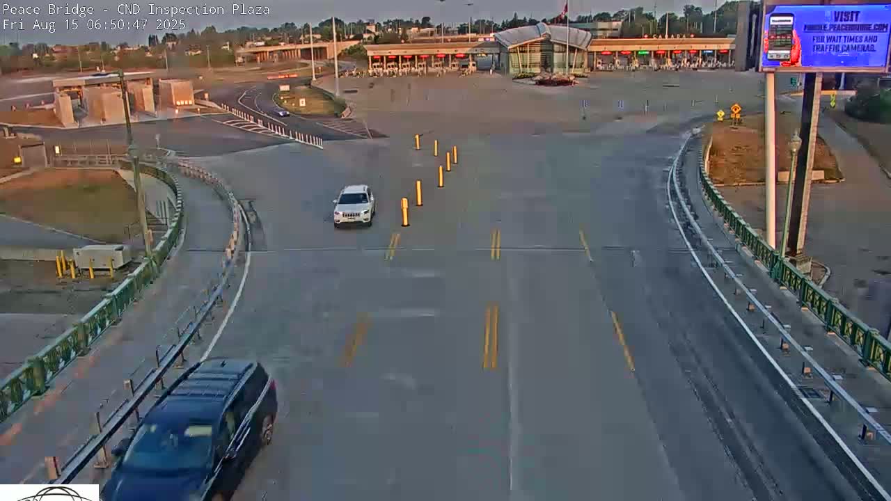 A nighttime, empty roadway curves toward a border inspection plaza under artificial light.