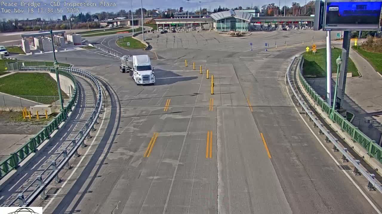 A nighttime, empty roadway curves toward a border inspection plaza under artificial light.