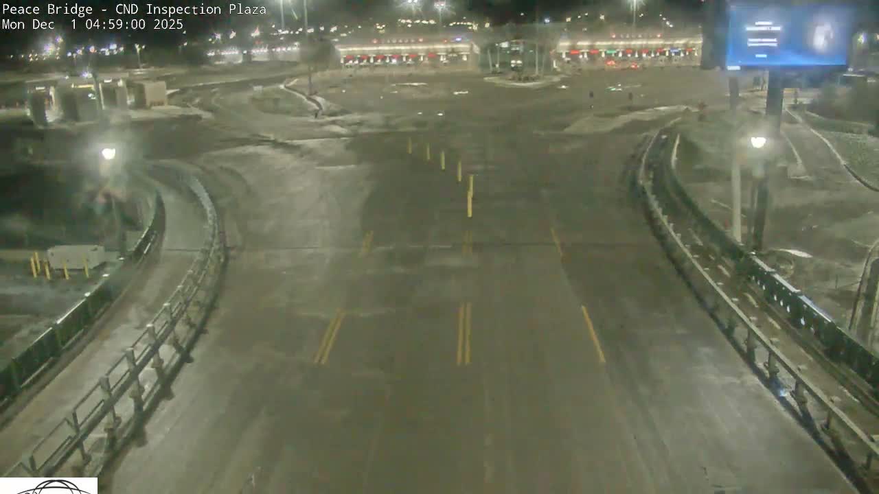 An elevated view shows a wet, multi-lane highway or bridge with curved ramps and distant buildings, illuminated by artificial lights on a clear, damp night.