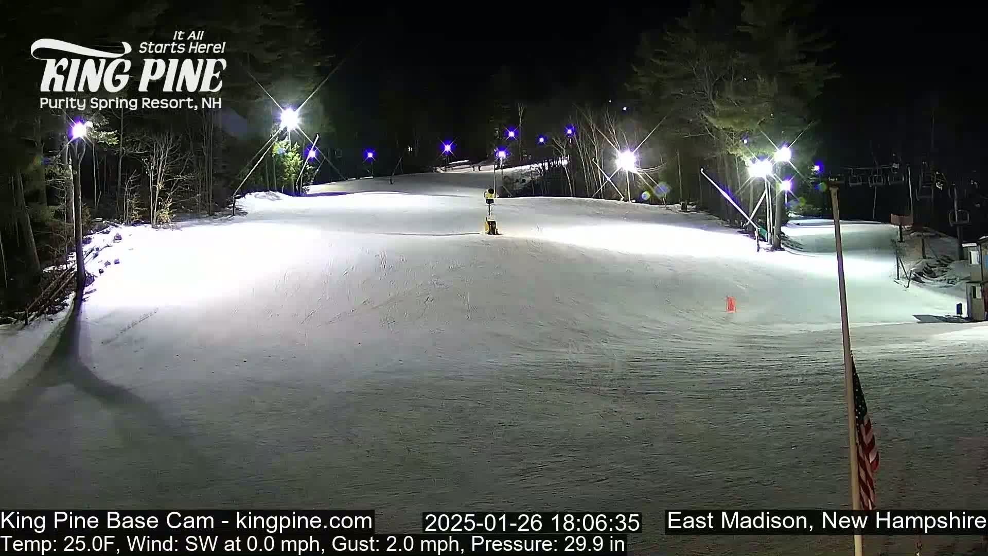 A snow-covered ski slope is illuminated at night by several bright lights.