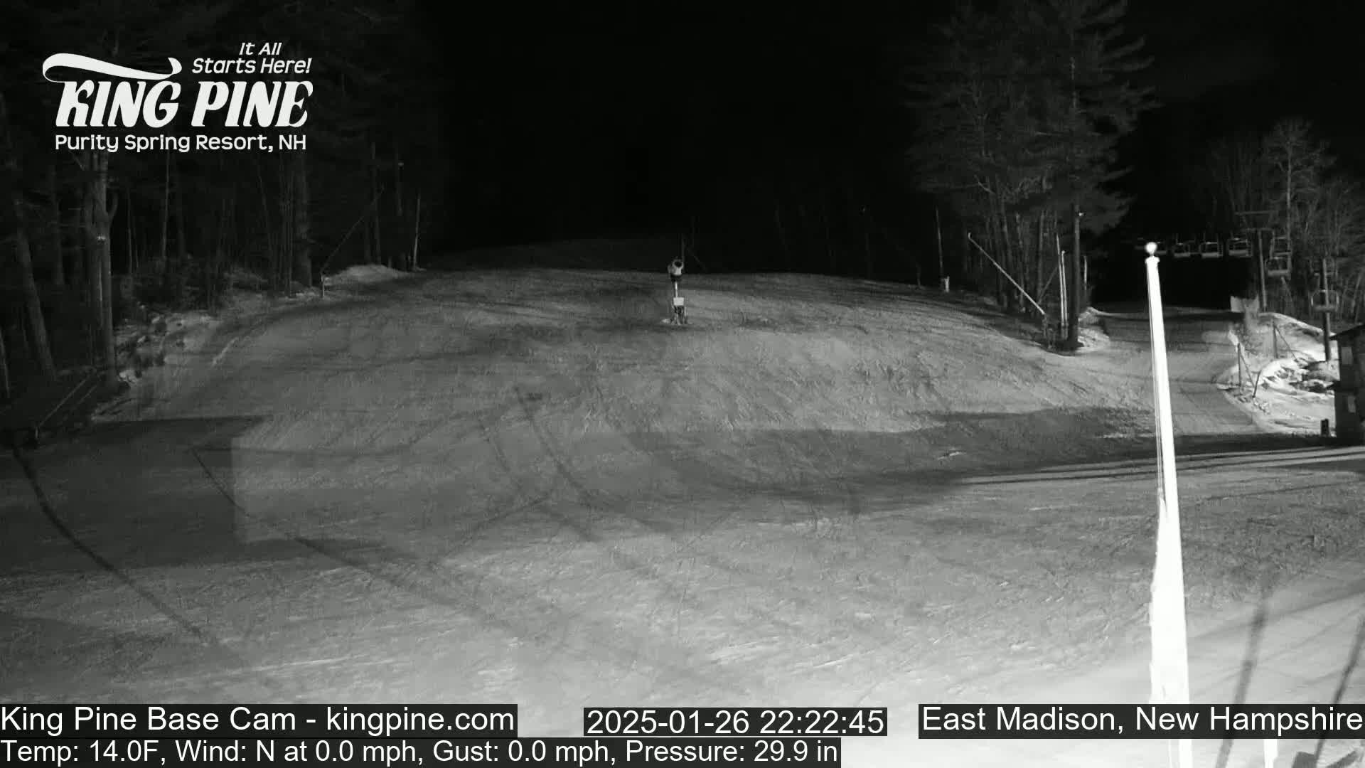 A nighttime, snow-covered ski slope is mostly empty except for one person near a lift.