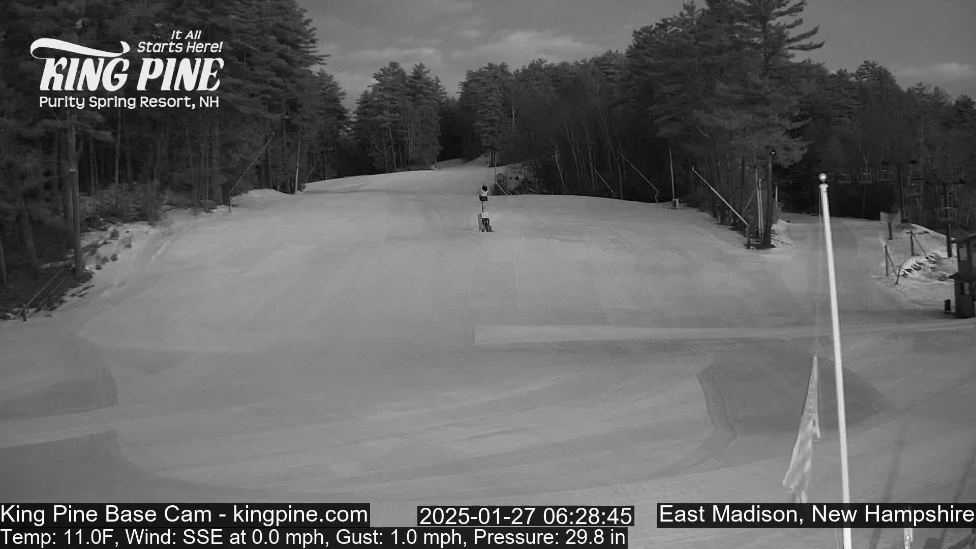 A snow-covered ski slope is visible, with a person standing near a lift in the background under a mostly cloudy sky.
