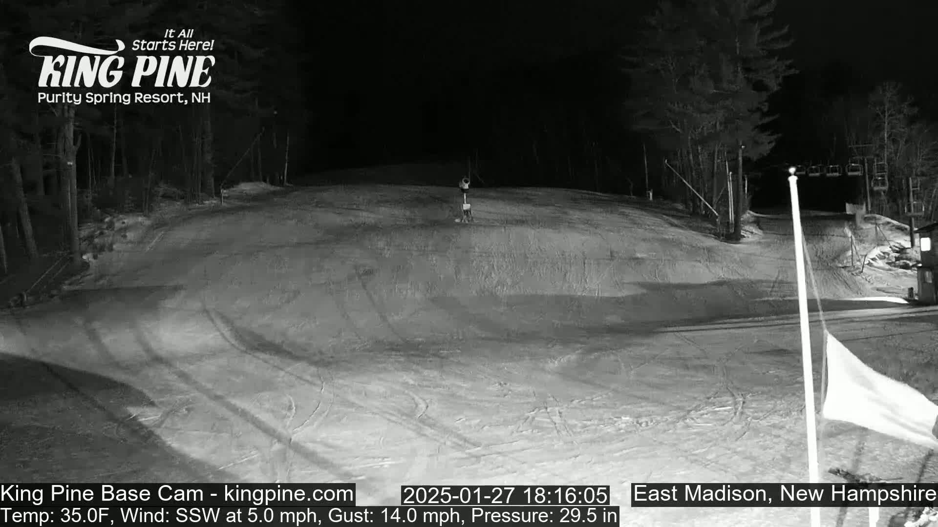 A nighttime view of a snow-covered ski slope with trees in the background under a clear, dark sky.
