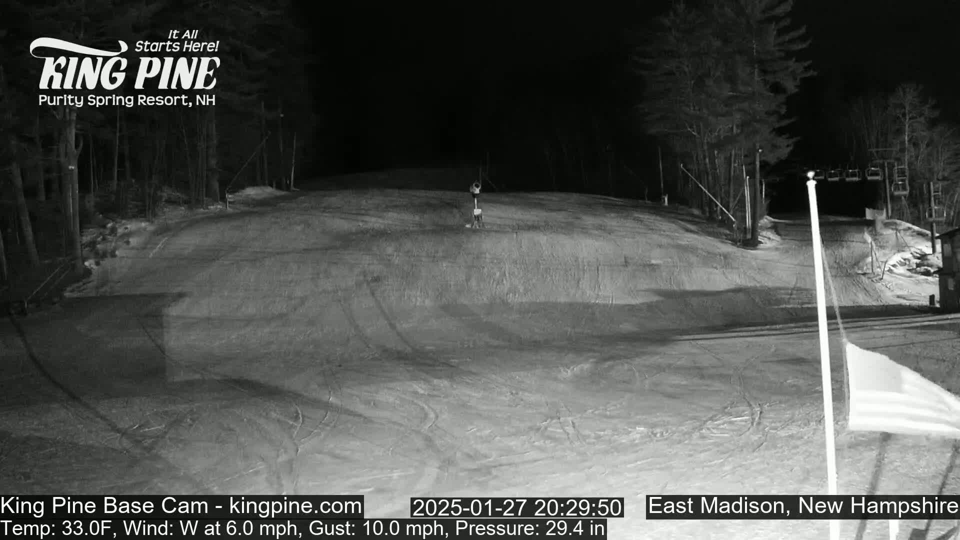 A nighttime, snow-covered ski slope is shown under a clear sky, with a chairlift visible in the background.