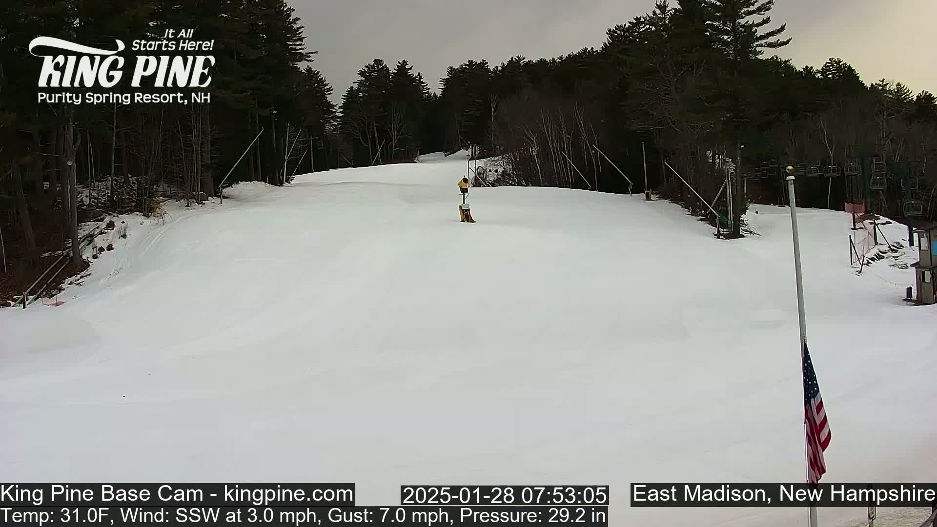 A snow-covered ski slope is seen under an overcast sky, with a person visible near a lift in the distance.