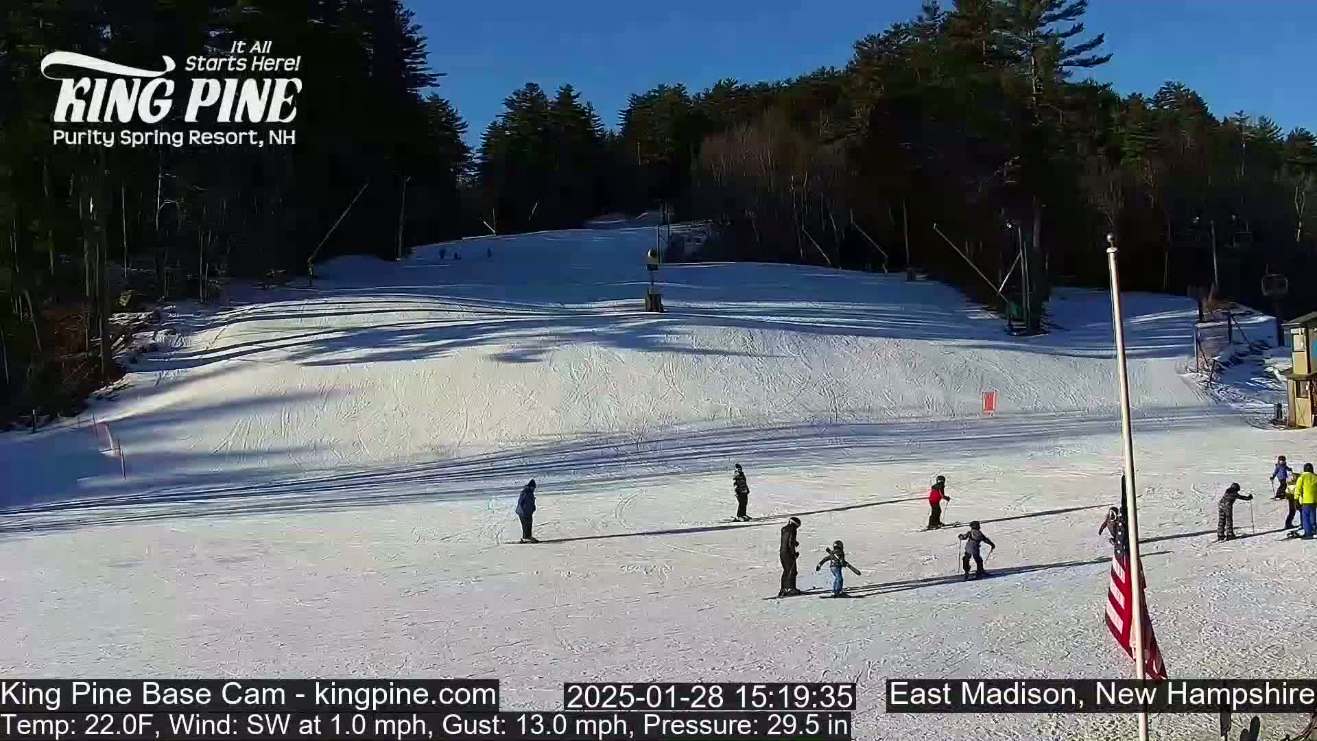 A snow-covered ski slope with several skiers and snowboarders on it under a sunny sky.