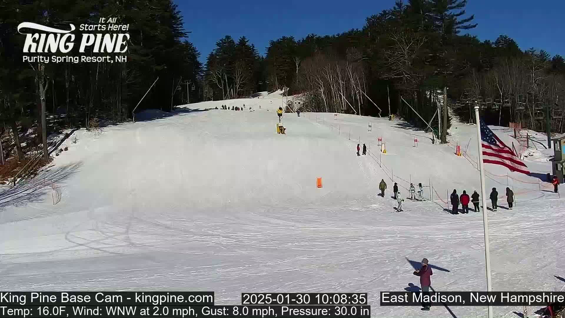 A snow-covered ski slope with skiers and onlookers, under a sunny sky.