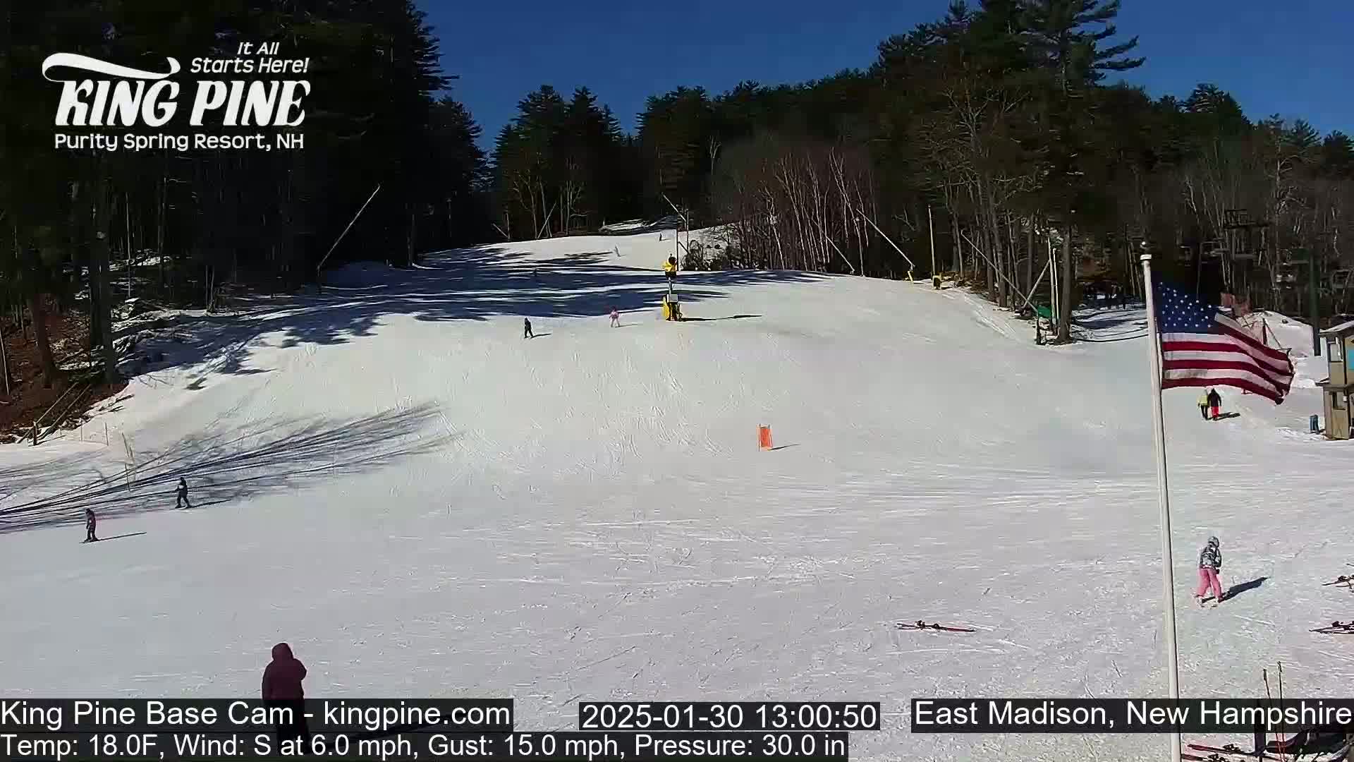 A snow-covered ski slope with several skiers visible on a sunny day.