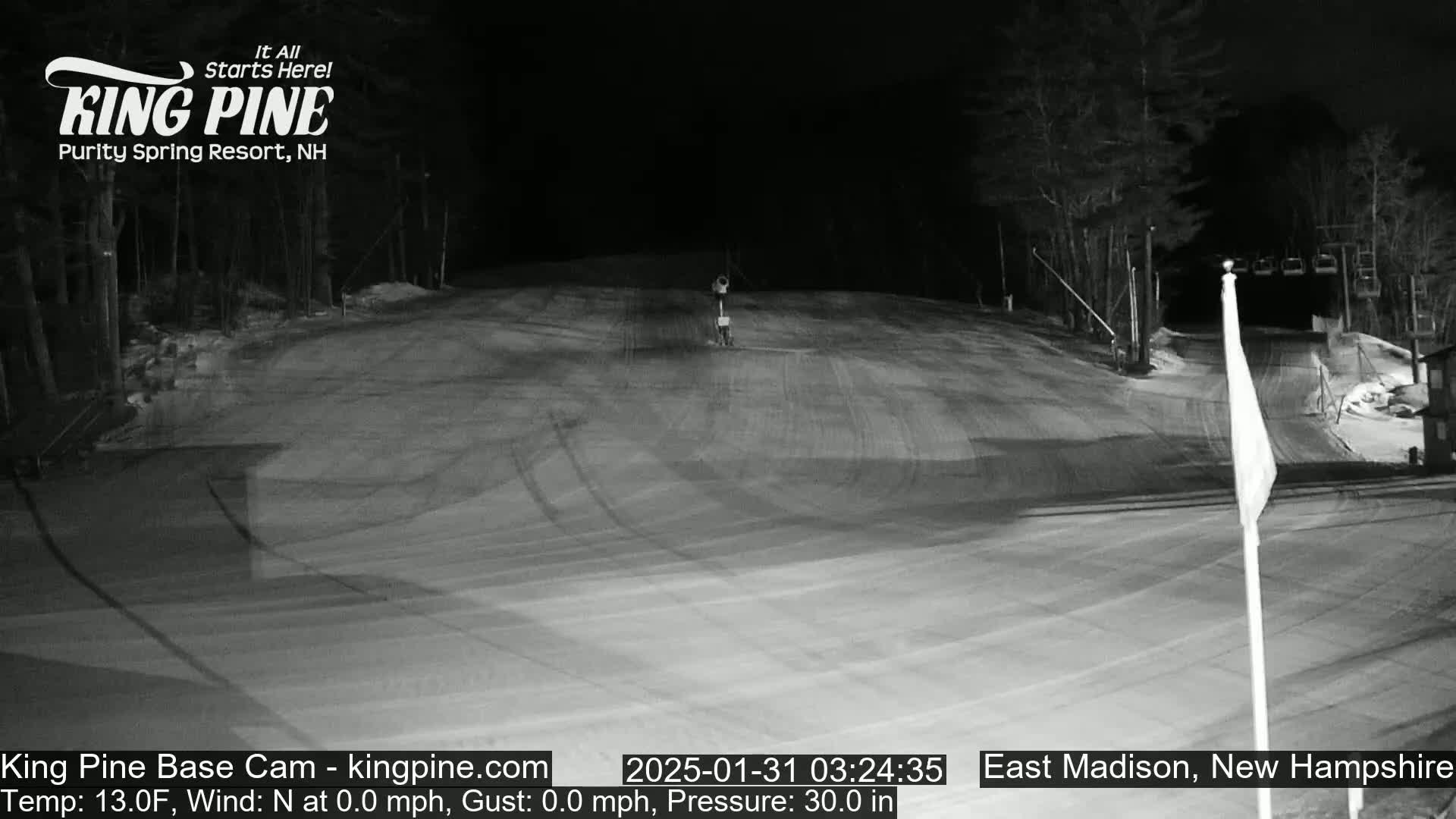 A snow-covered ski slope at night with a chairlift in the background under a clear, dark sky.