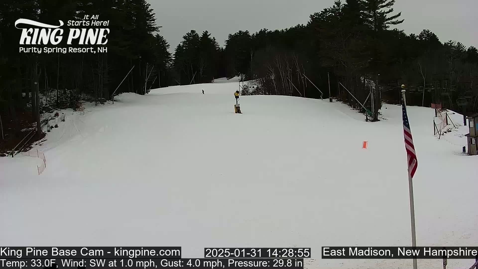 A mostly clear, snowy ski slope with a few skiers visible, under an overcast sky.