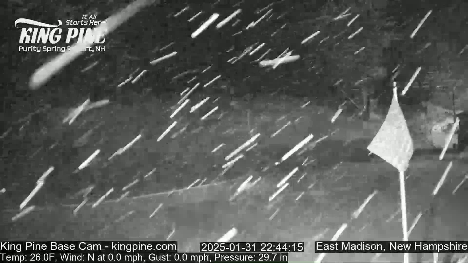 A nighttime snowstorm is falling over a partially visible flagpole.