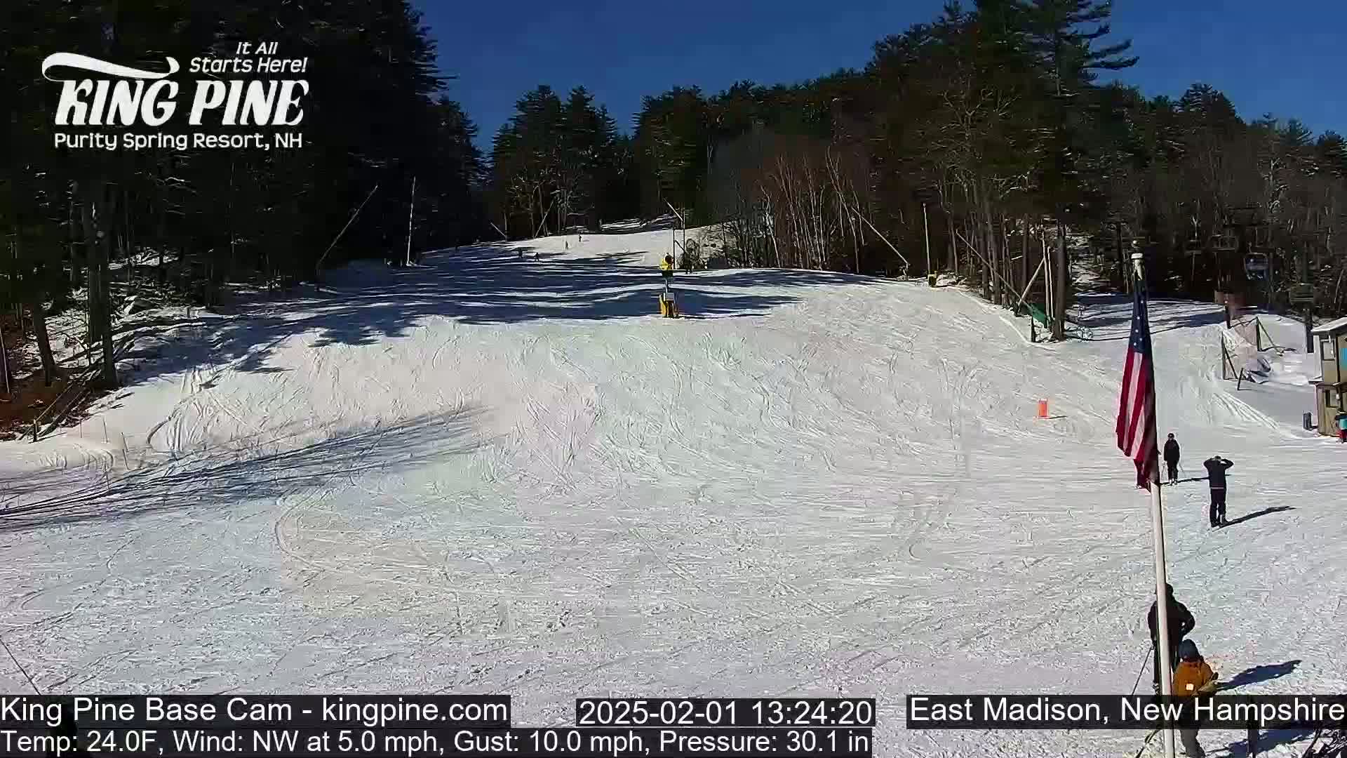 A snow-covered ski slope on a sunny day with a few skiers and a flagpole with an American flag.