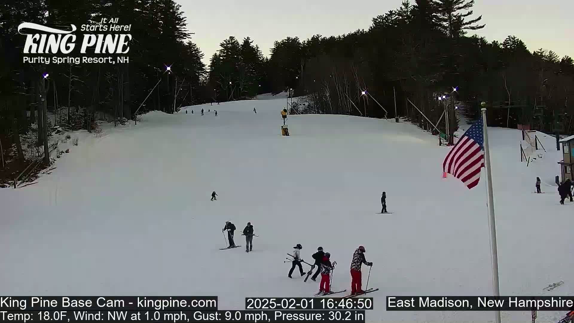 A snow-covered ski slope with several skiers and snowboarders, under a twilight sky.