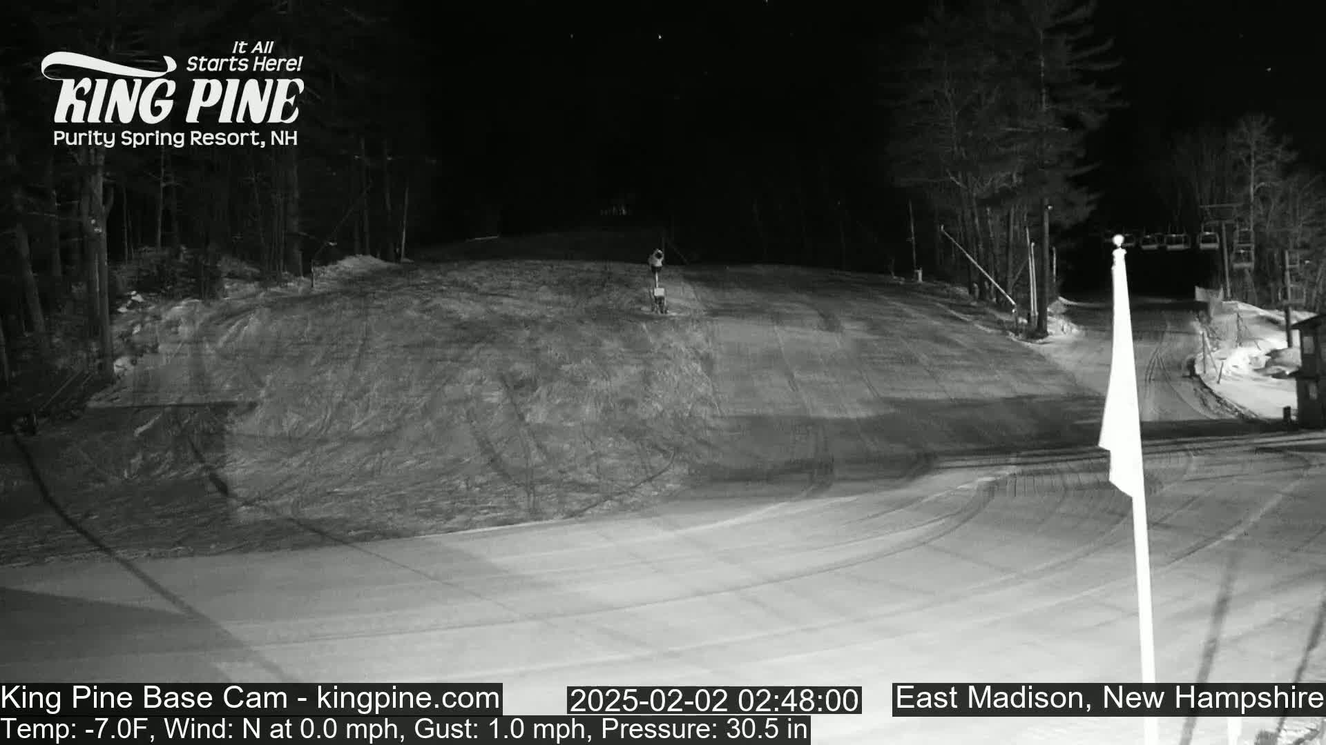 A nighttime view of a snow-covered ski slope with a chairlift visible in the background under a clear, dark sky.