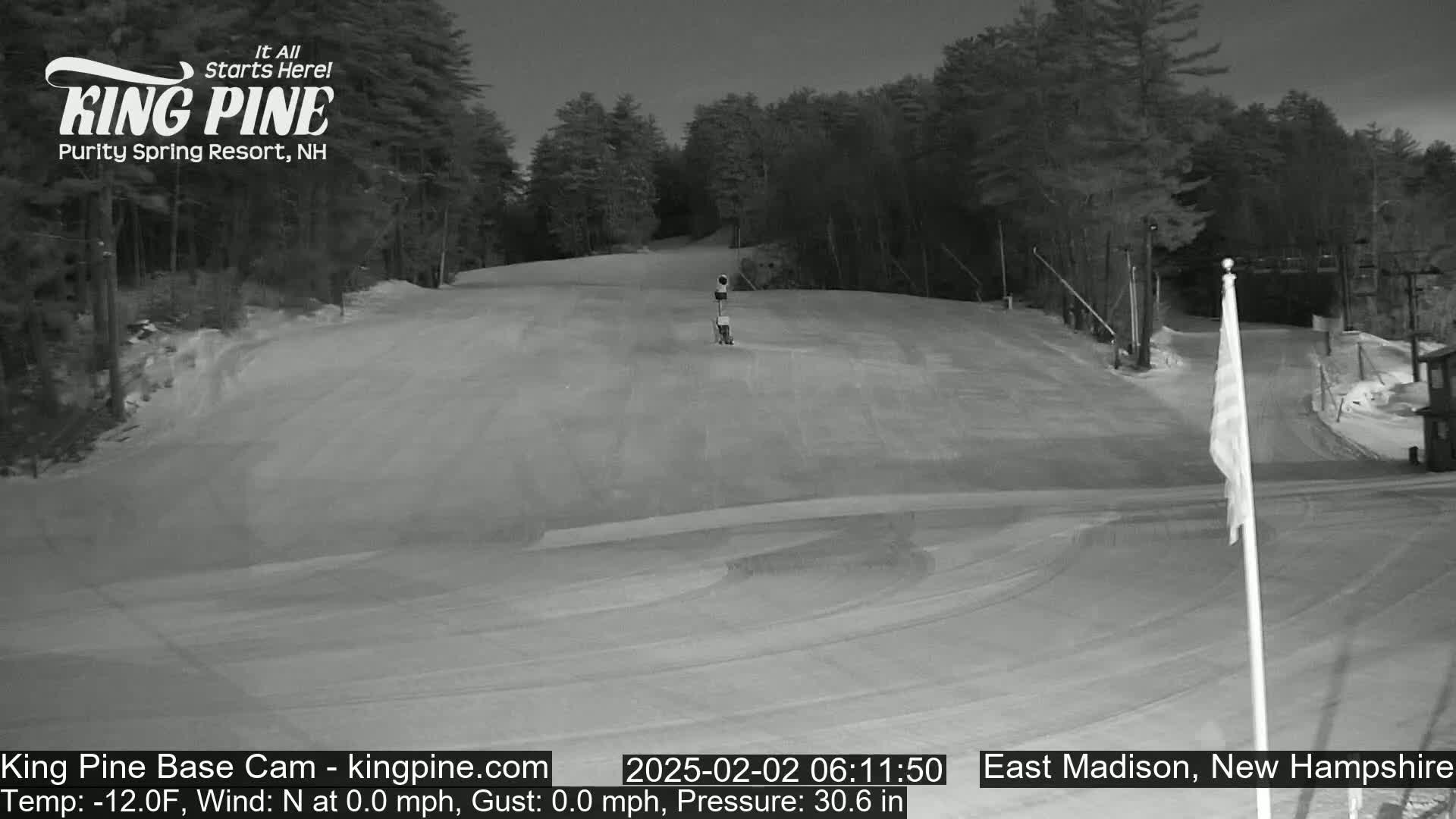 A snow-covered ski slope at night, under a dark sky, is illuminated by artificial light.