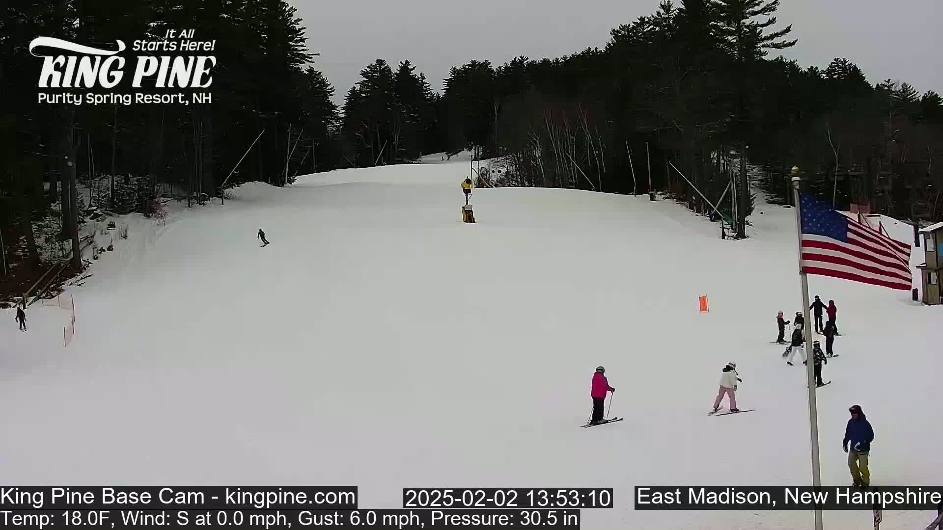 A snow-covered ski slope with several skiers and snowboarders, under an overcast sky.