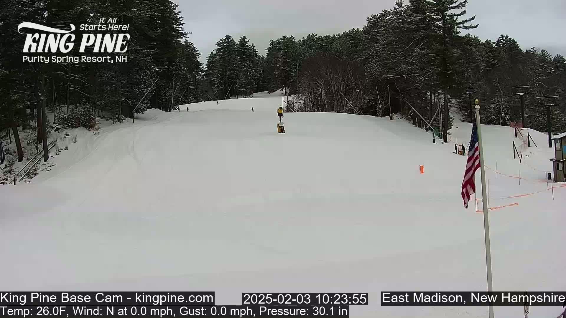 A snow-covered ski slope with a few skiers is visible beneath an overcast sky.