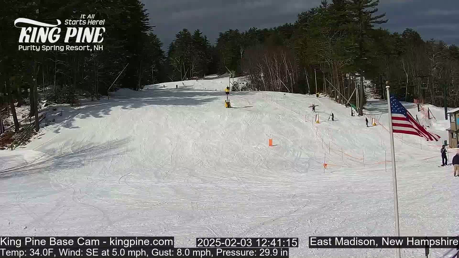 A snow-covered ski slope with several skiers and a partially sunny sky.