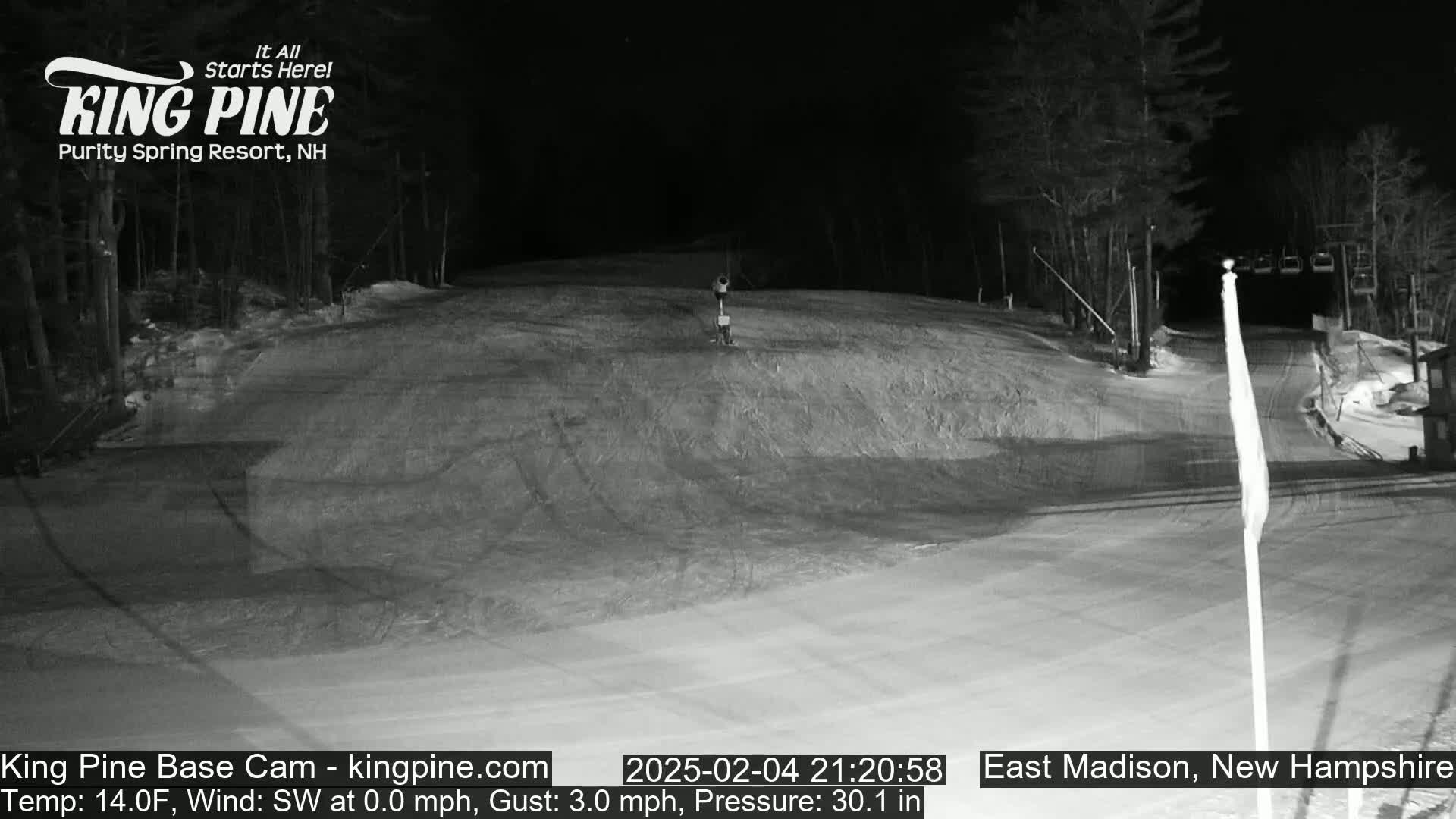 A nighttime view of a snow-covered ski slope with a chairlift in the background under a dark sky.
