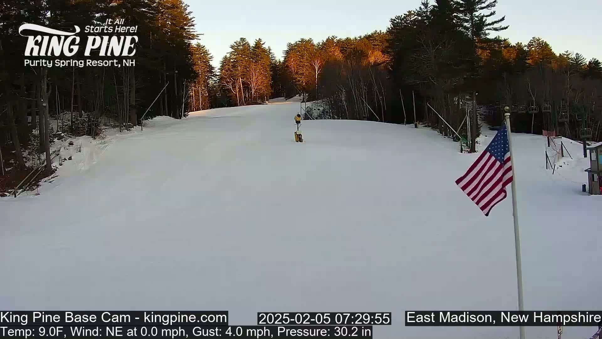 A snow-covered ski slope is visible, with a person skiing down the middle, under a clear, bright sky, and a US flag standing in the lower right corner.