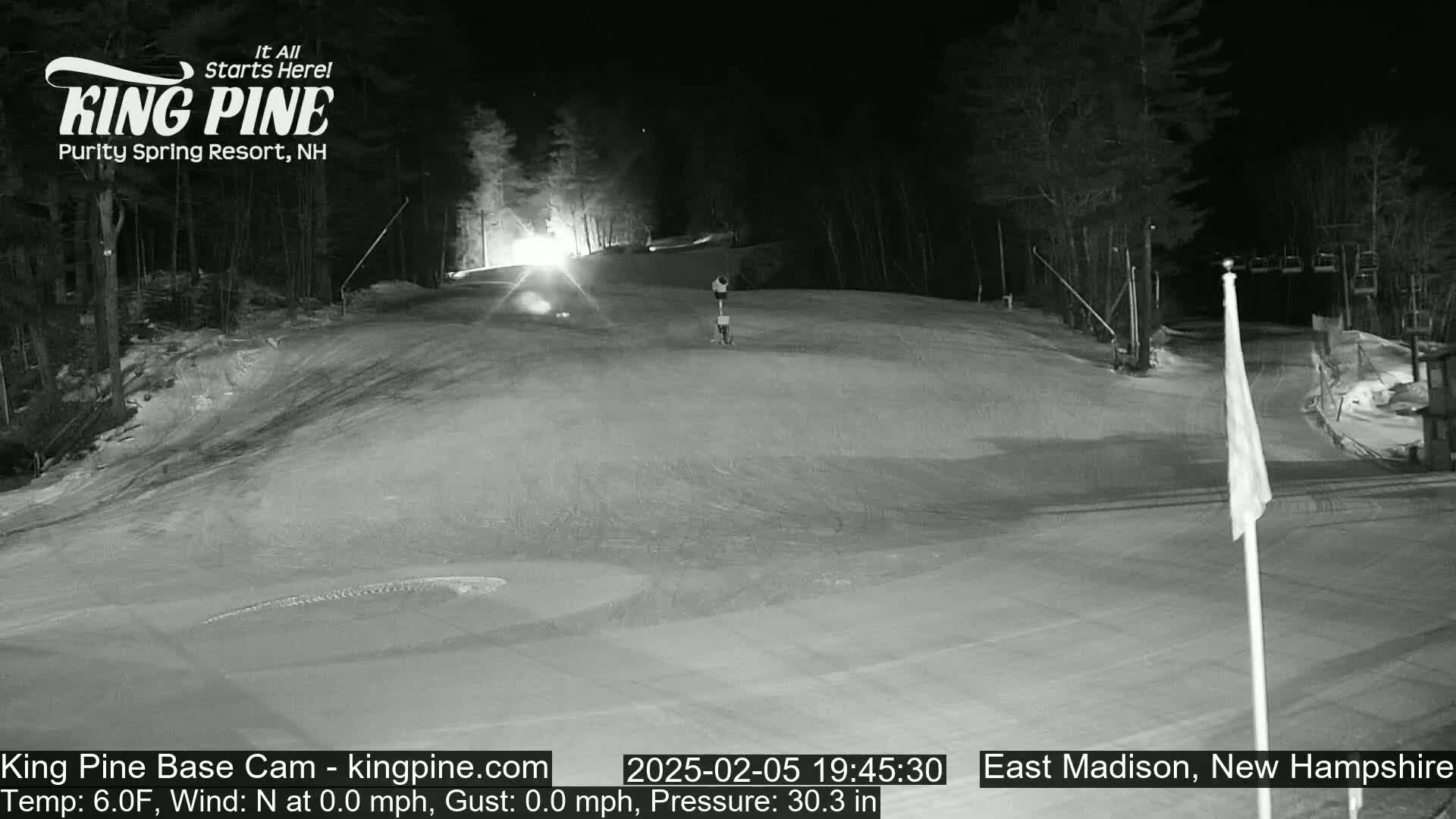 A nighttime view of a snow-covered ski slope with a single person visible, under a clear sky.