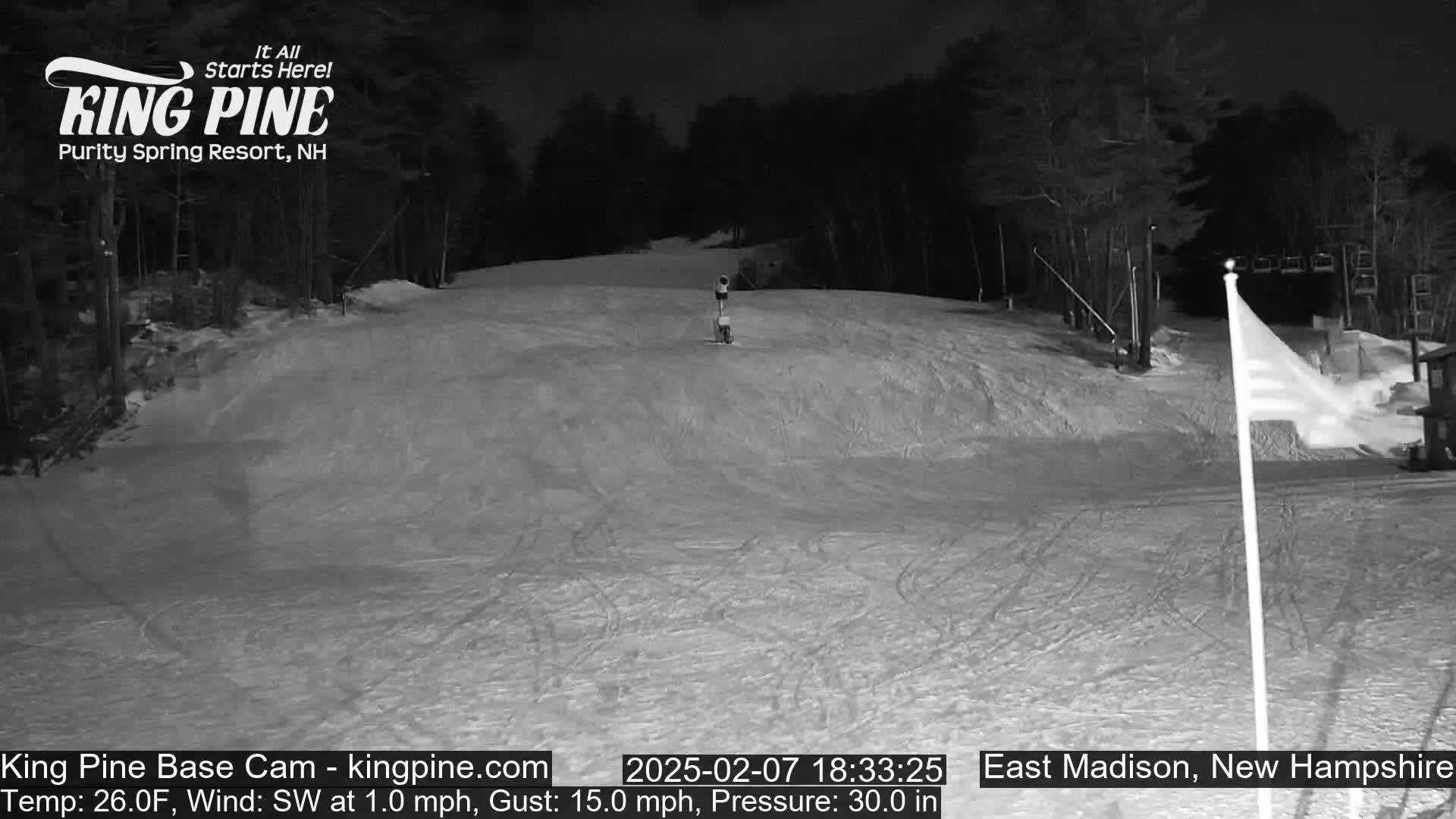 A nighttime view of a snow-covered ski slope with trees in the background under a dark sky.