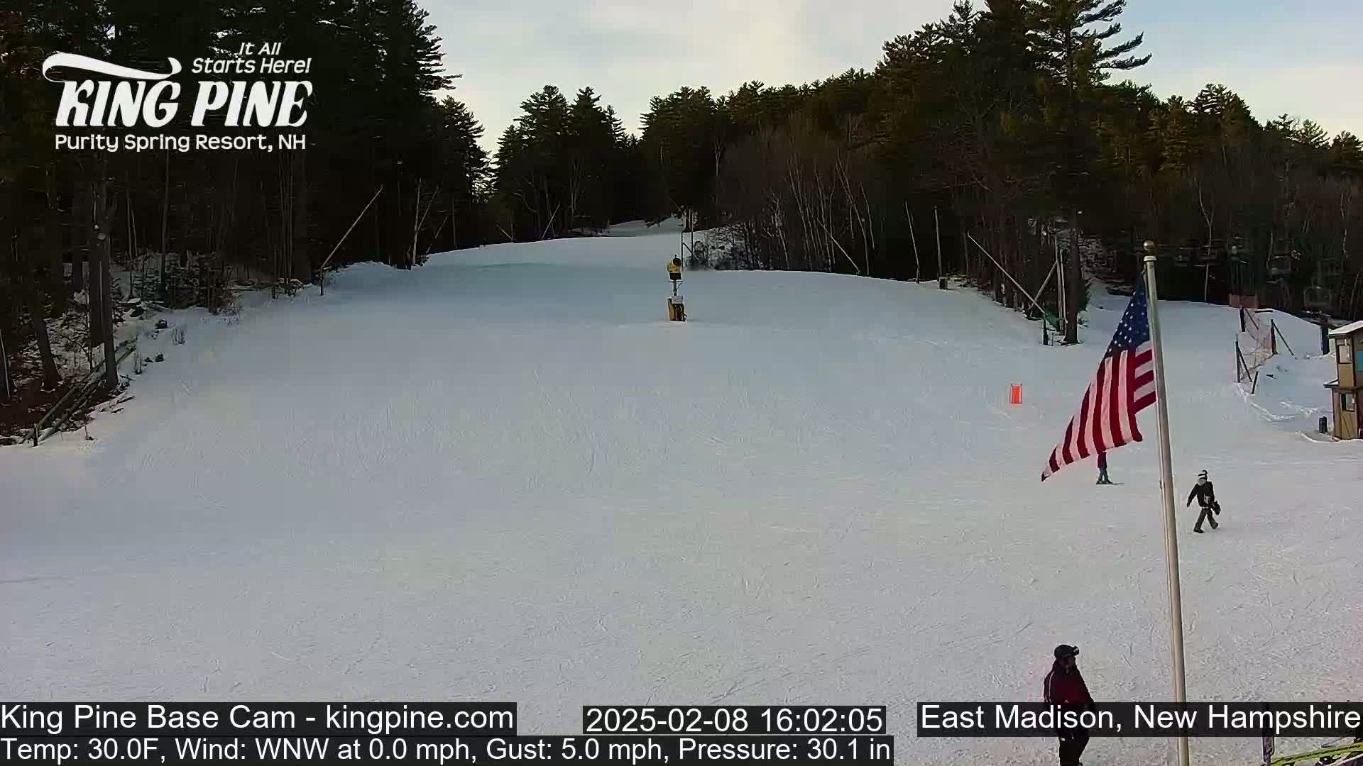 A snowy ski slope with several skiers and a US flag is visible under a partly cloudy sky.