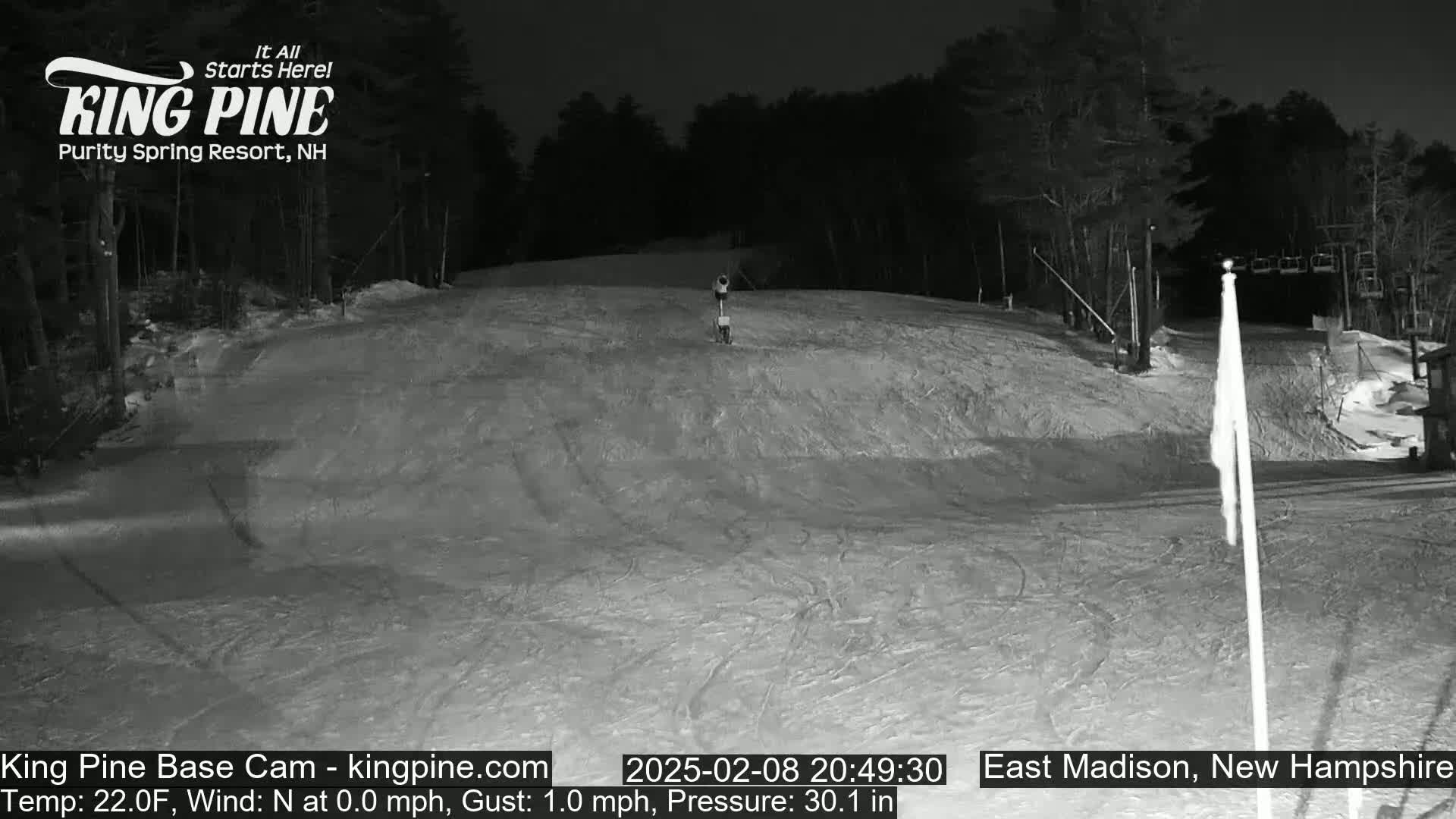 A nighttime view of a snow-covered ski slope with a chairlift in the background under a clear sky.