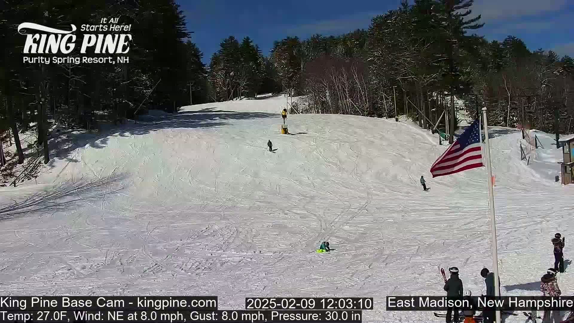 A snow-covered ski slope with several skiers and snowboarders on a sunny day.