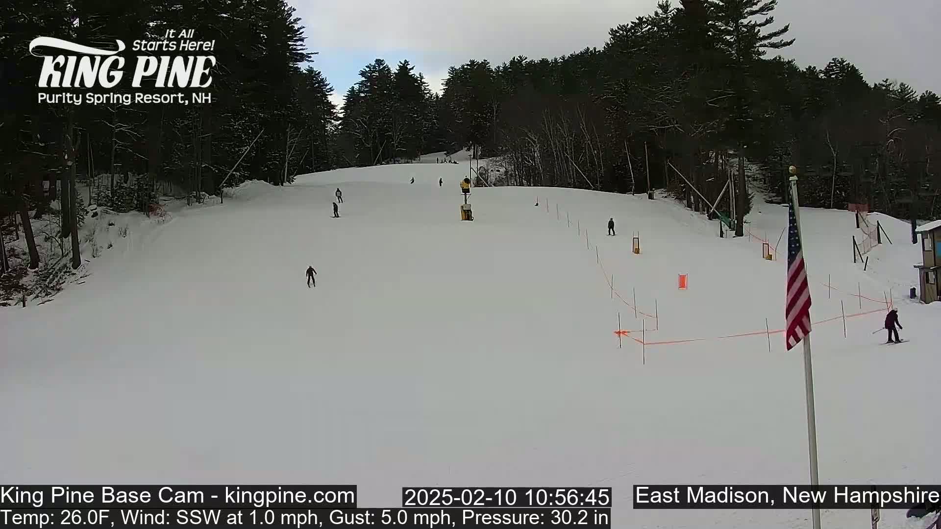 A snow-covered ski slope with several skiers and a partially cloudy sky.