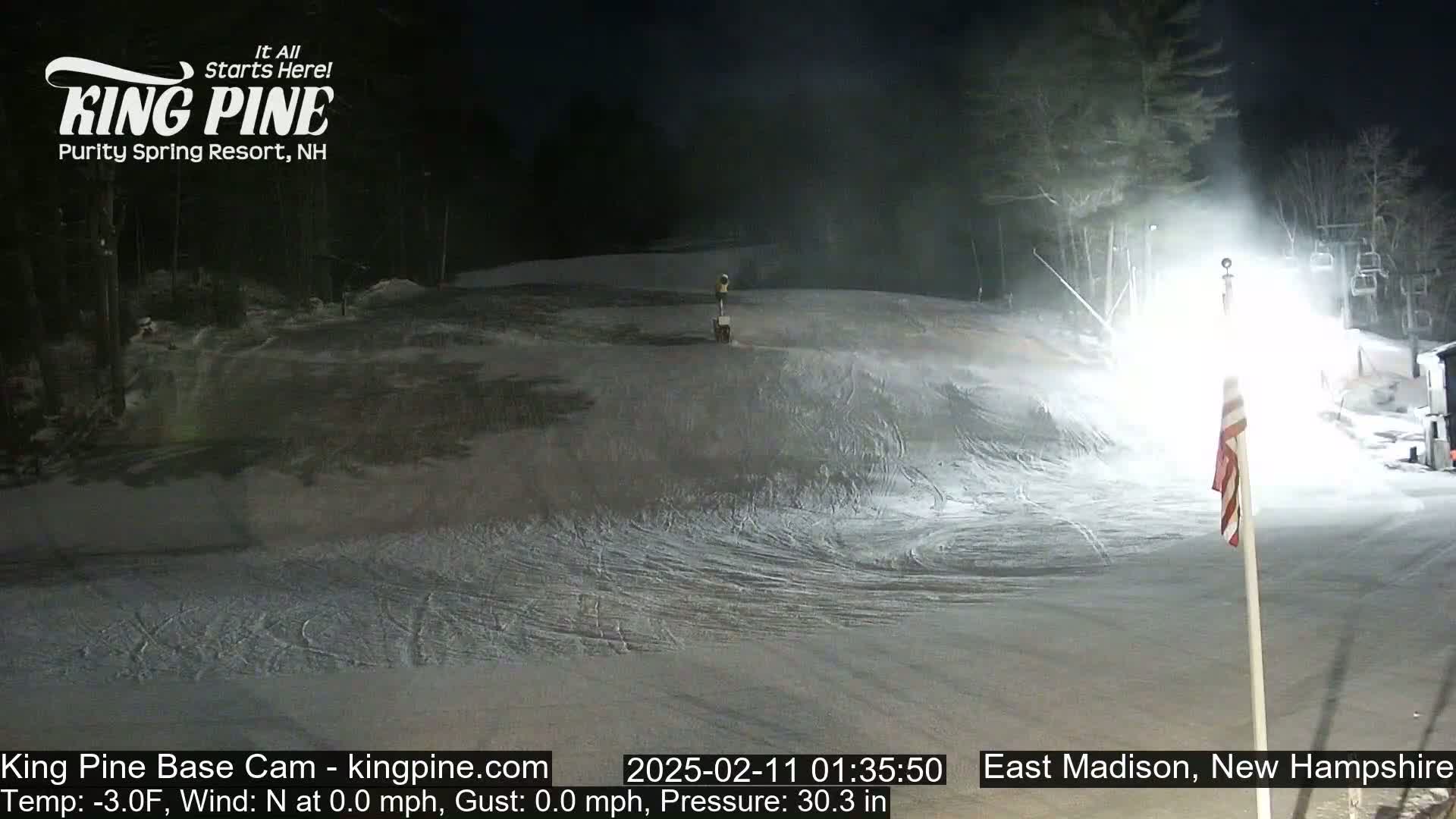 A snow-covered ski slope at night, illuminated by bright lights, with a calm wind and a temperature of -3.0°F.