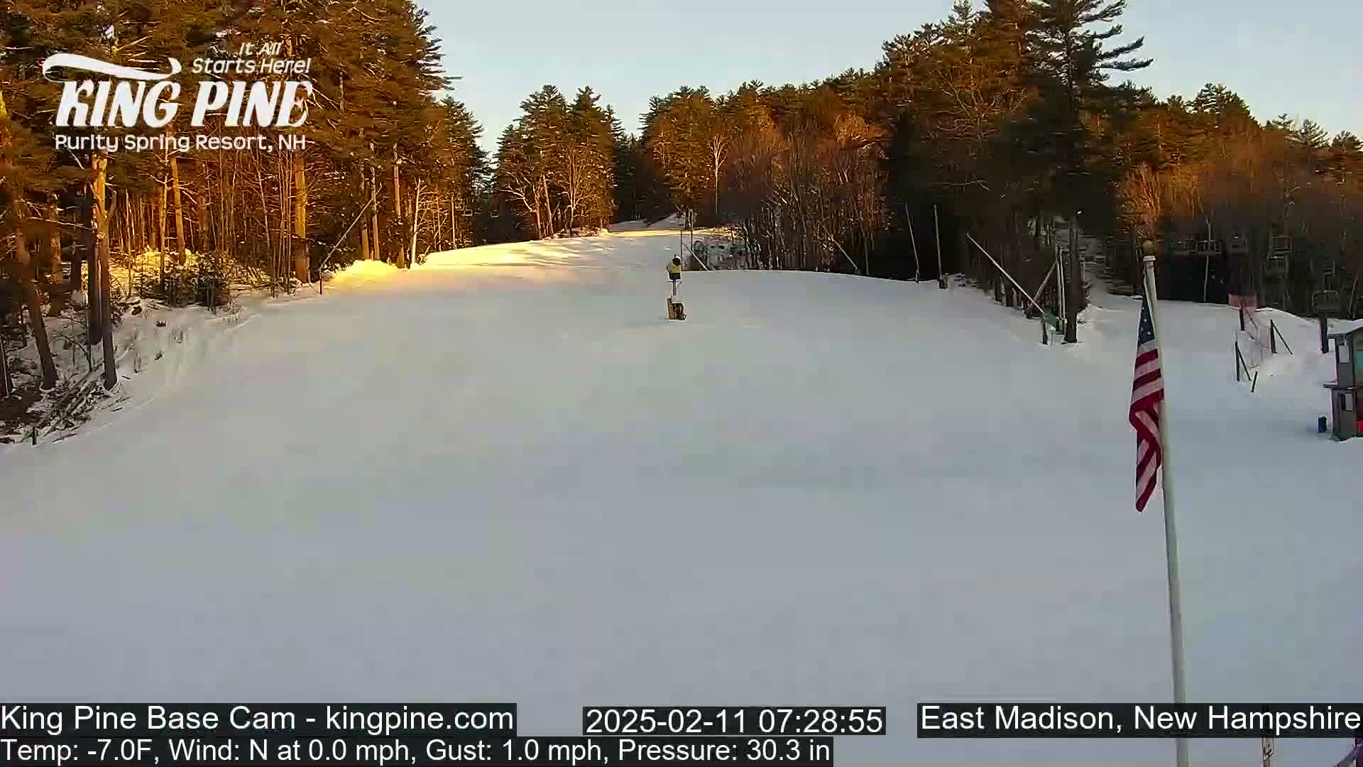 A person skis down a snow-covered slope at a ski resort, under a clear, sunrise sky.