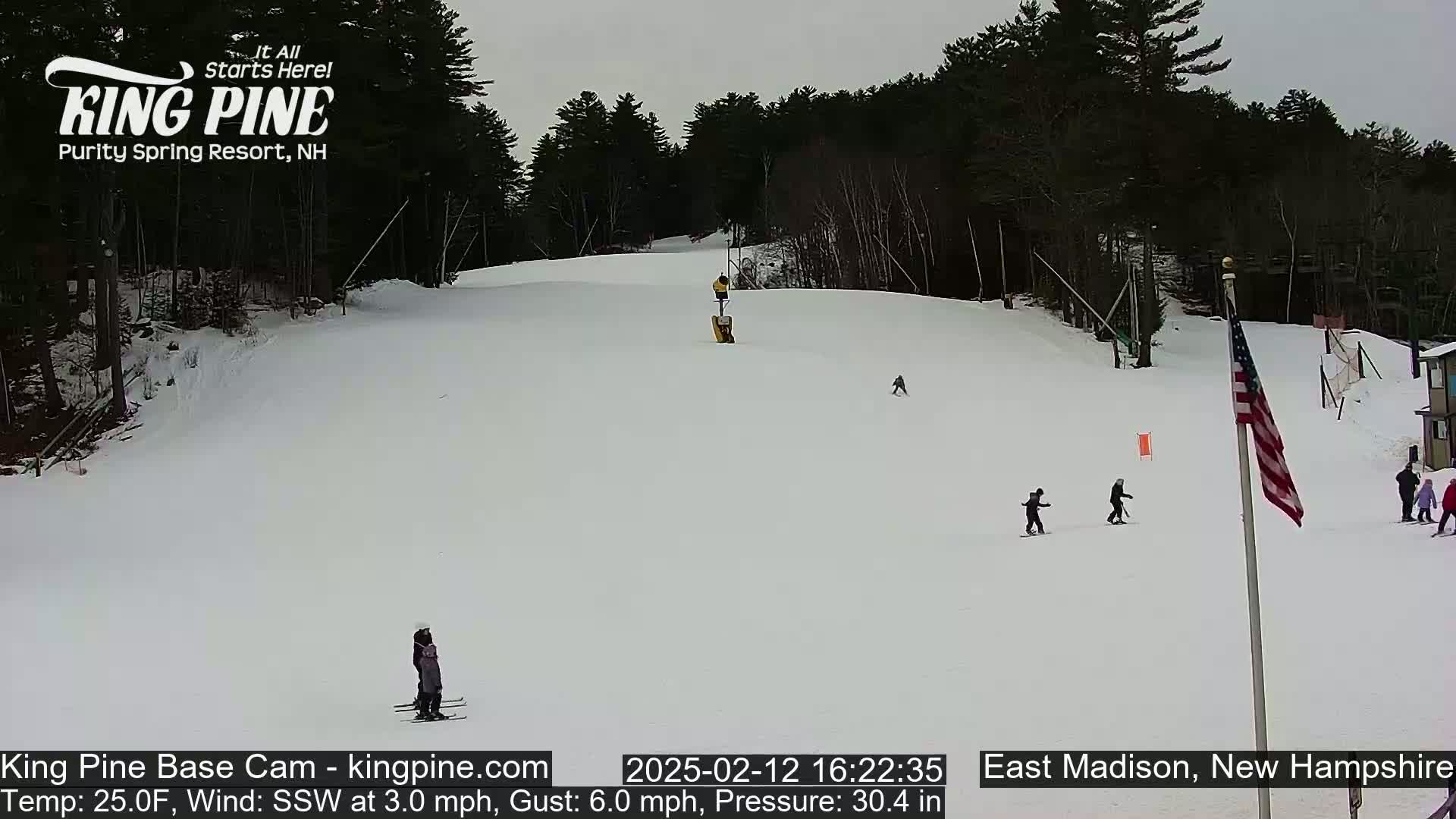 A snow-covered ski slope with several skiers and snowboarders, under an overcast sky.