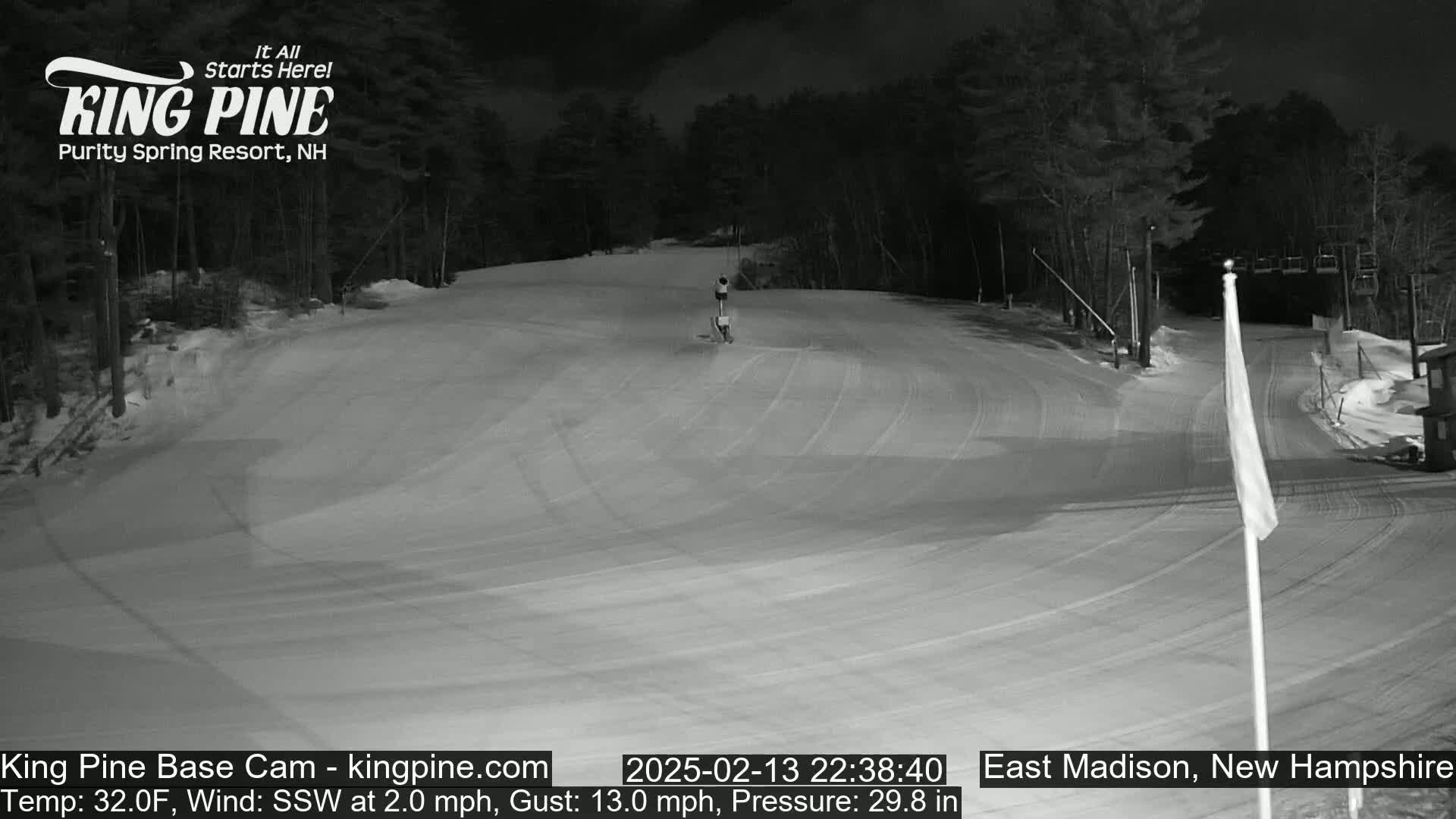 A nighttime view of a snow-covered ski slope with a person skiing down, under a dark sky.