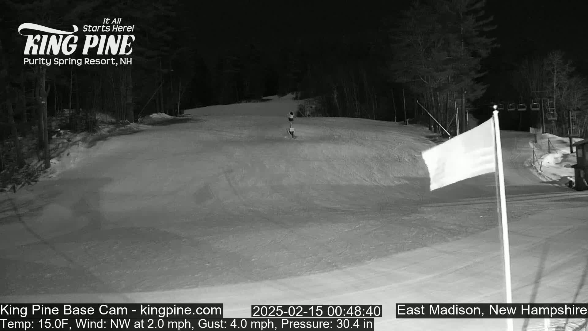 A nighttime view of a snow-covered ski slope with a person skiing down it, under a dark sky with a northwest wind at 2.0 mph and a 4.0 mph gust.