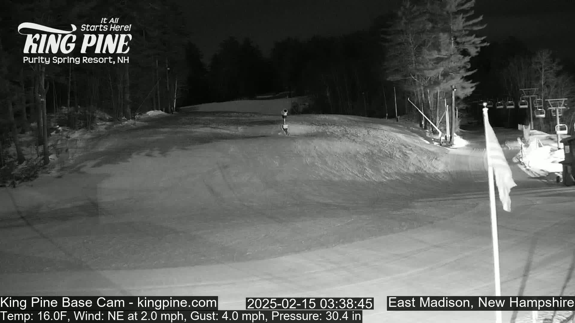 A snow-covered ski slope at night, illuminated by lights, with a person skiing down a hill, and ski lifts visible in the background.