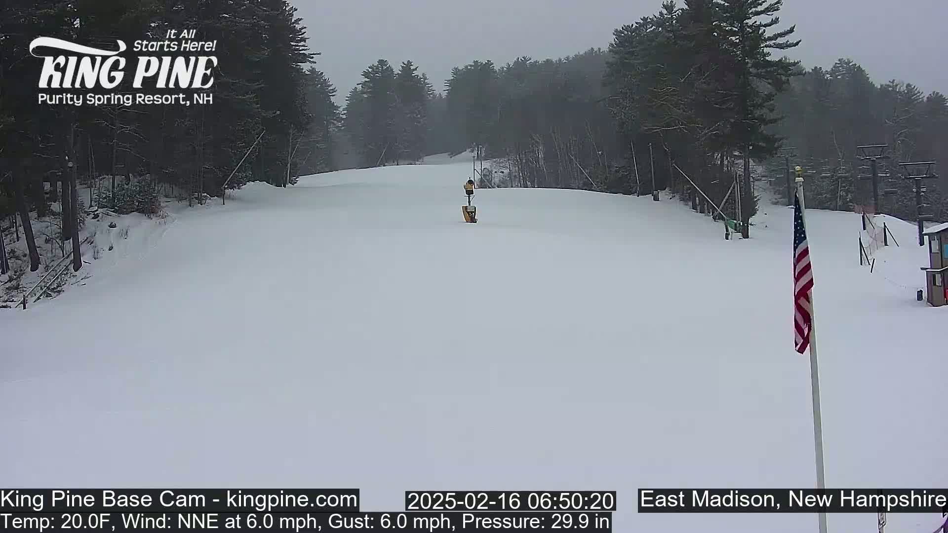 A snow-covered ski slope is visible, with a mostly overcast sky and a small piece of an American flag in the lower-right corner.
