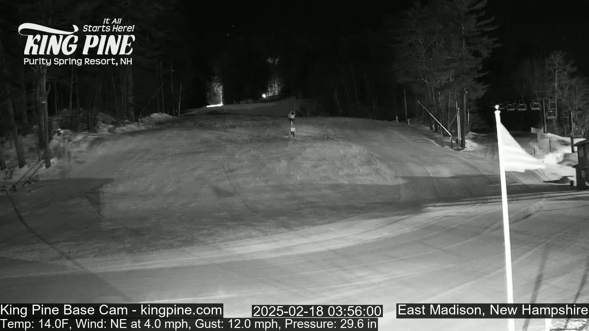 A snow-covered ski slope at night, illuminated by lights, with a northeast wind.