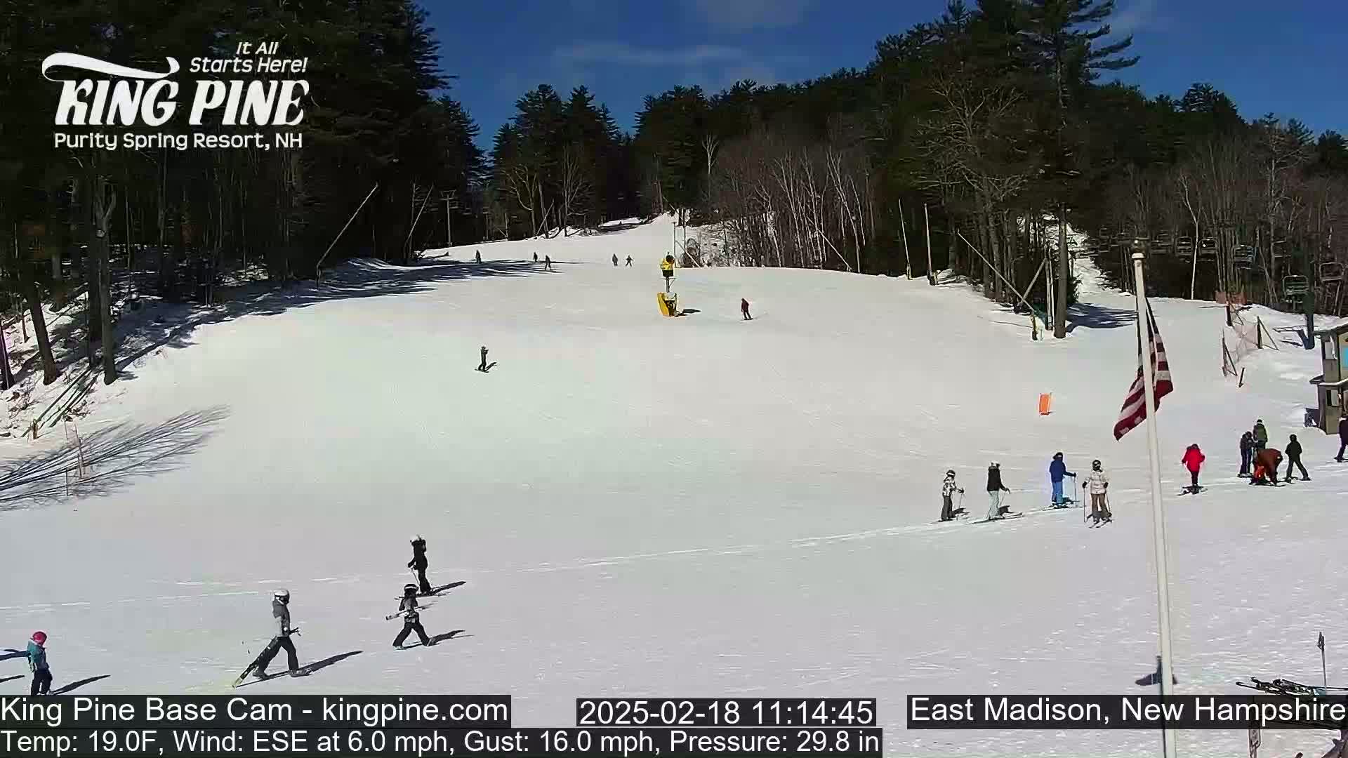 A snow-covered ski slope with several skiers and snowboarders on a sunny day.