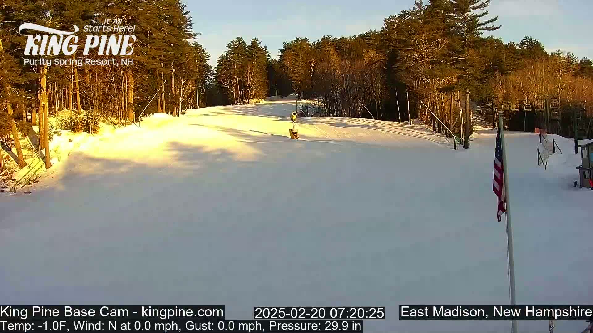 A snow-covered ski slope is visible at sunrise, with a calm wind and a mostly clear sky.