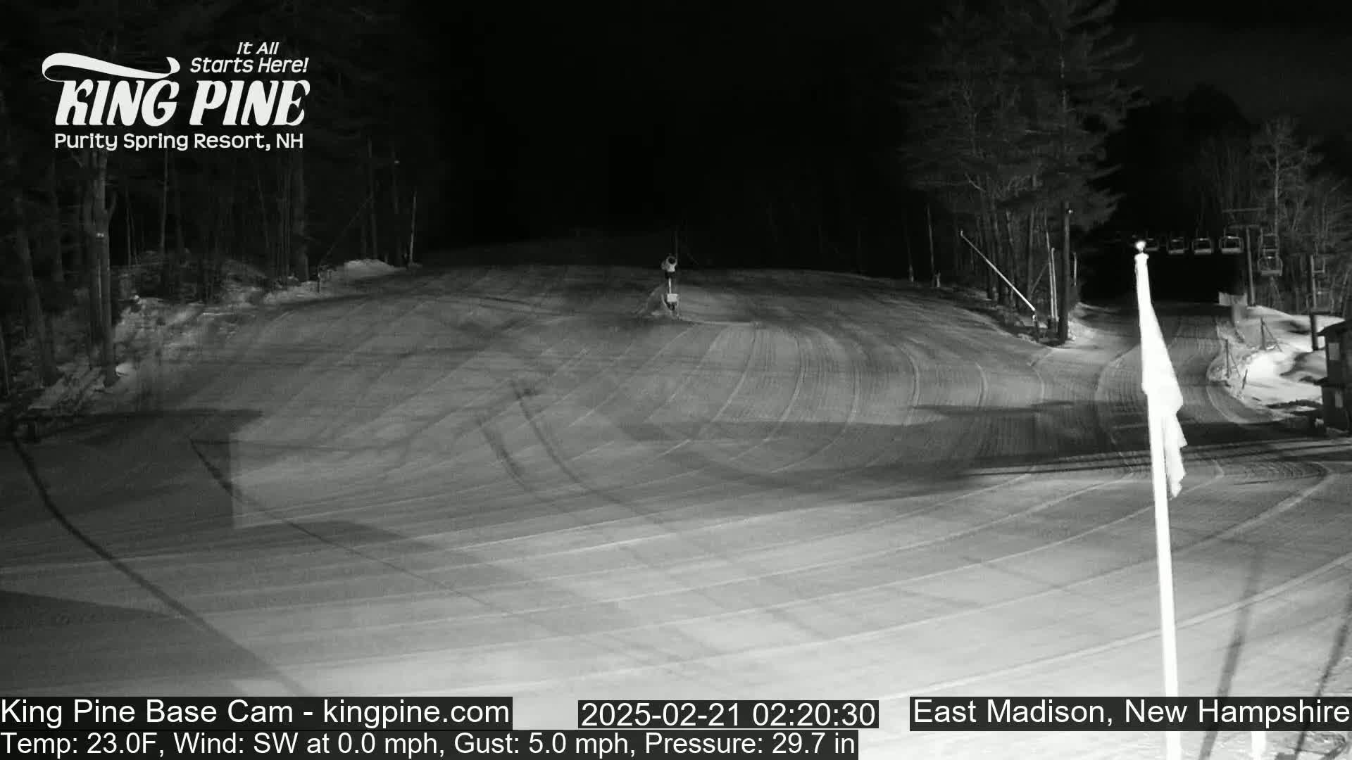 A nighttime, snow-covered ski slope is visible under a clear sky with a 23°F temperature and a southwest wind of 0 mph gusting to 5 mph.